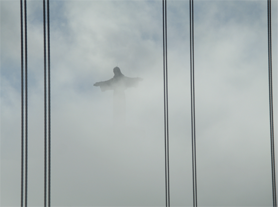 A estátua do Cristo Rei sob o manto do nevoeiro matinal, visto da Ponte 25 de Abril.